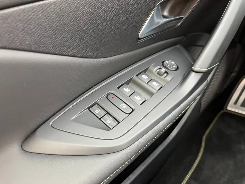 Gros plan sur la commande des vitres électriques côté conducteur du Peugeot 308 SW Bleu Avatar avec surpiqûres vertes sur la porte.