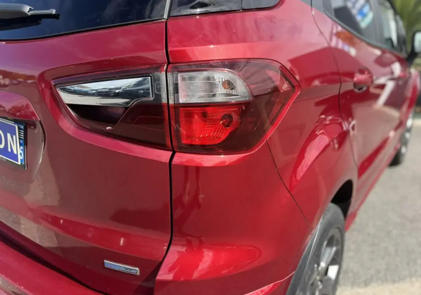 Gros plan sur le feu arrière droit d'une Ford EcoSport rouge métallisée, soulignant la finition EcoBlue et la carrosserie brillante.