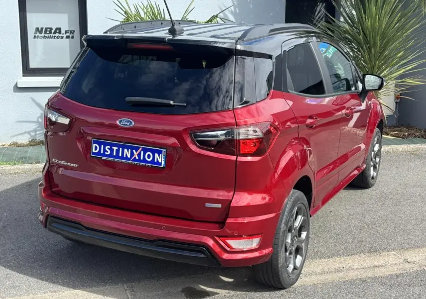 Vue 3/4 arrière droite d'un Ford EcoSport rouge métallisé avec vitres arrière surteintées et barres de toit noires.