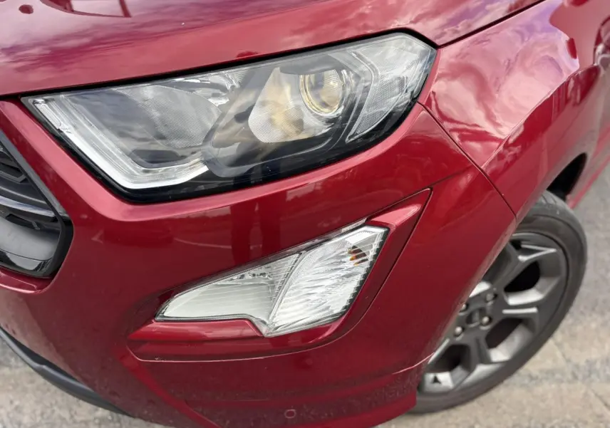 Gros plan sur le phare avant droit et la roue alliage 17 pouces du Ford EcoSport rouge métallisé.