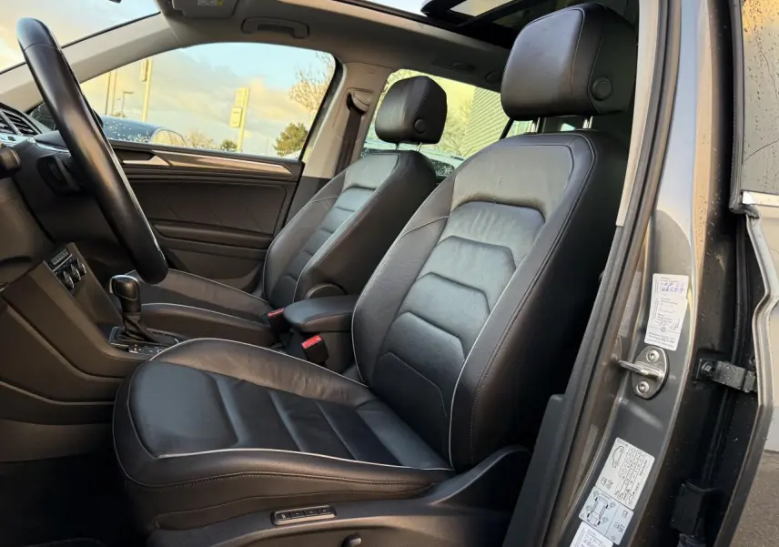 Vue intérieure côté gauche du Volkswagen Tiguan 2019, sièges sport cuir noir et toit ouvrant panoramique visibles.