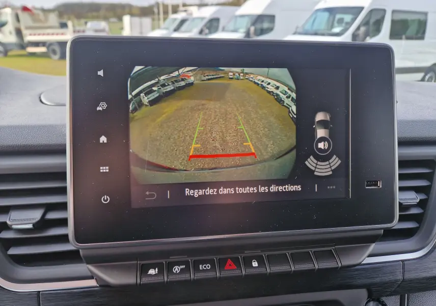 Écran central du Nissan Primastar blanc montrant la caméra de recul avec vue arrière et lignes de guidage colorées.