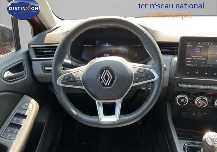 Vue intérieure centrée sur le volant Renault Clio V rouge flamme, avec tableau de bord digital et console tactile visible.