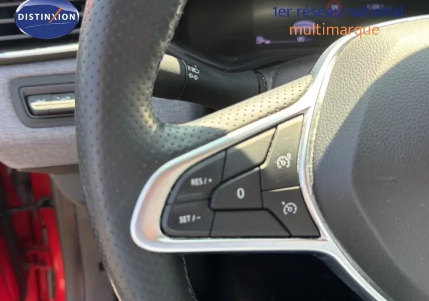 Gros plan sur les commandes au volant côté gauche de la Renault Clio V rouge flamme, avec boutons de régulateur de vitesse.