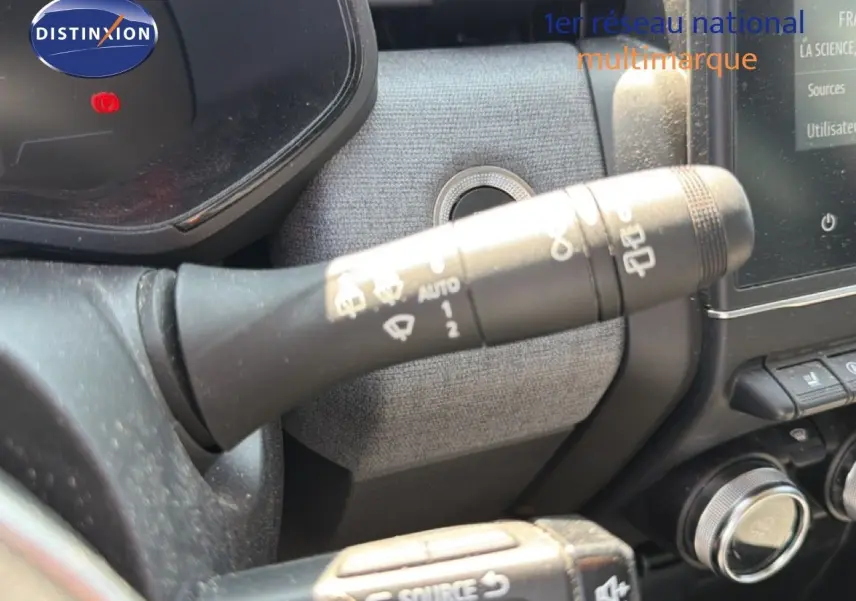 Gros plan sur la commande des essuie-glaces à gauche du volant dans l'habitacle d'une Renault Clio V rouge flamme.