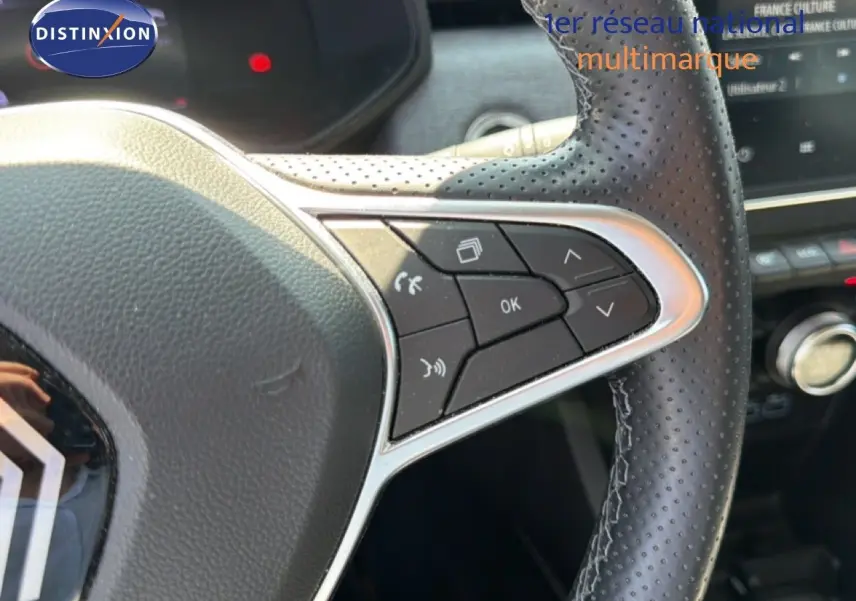 Gros plan sur le volant en cuir perforé de la Renault Clio V rouge flamme, avec commandes multifonctions visibles.