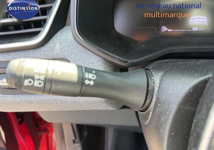 Gros plan sur la commande des phares à gauche du volant dans l’habitacle rouge flamme d’une Renault Clio V Evolution TCe 90.