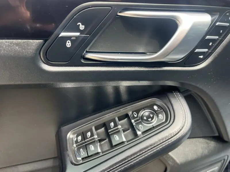 Gros plan sur la poignée de porte intérieure et les commandes des vitres côté conducteur du Porsche Macan noir de 2018.