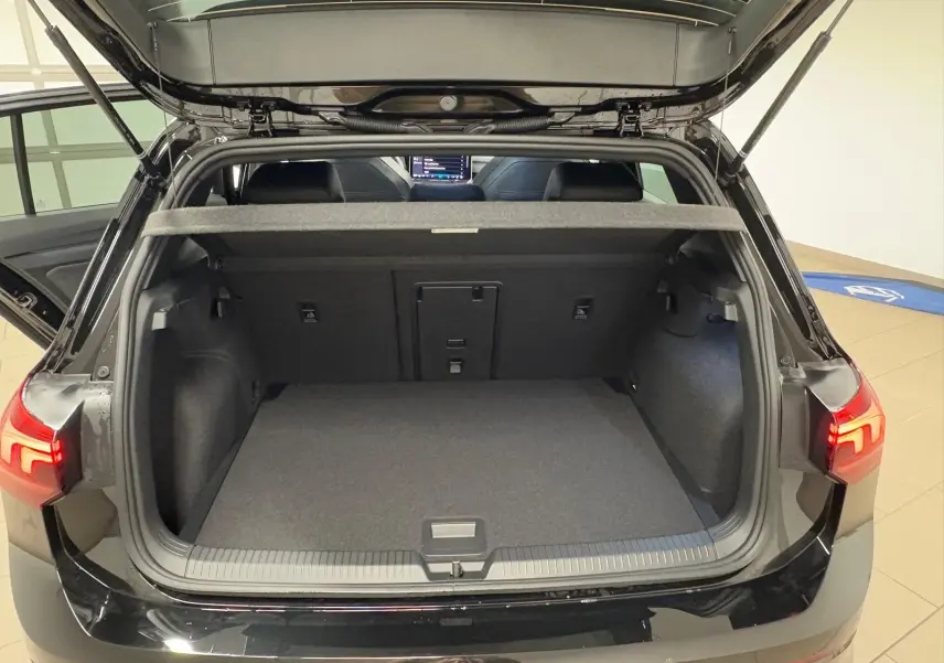Vue arrière du coffre ouvert d'une Volkswagen Golf 2.0 TDI noire Grenadille, montrant l'espace de chargement vide et les feux arrière allumés.