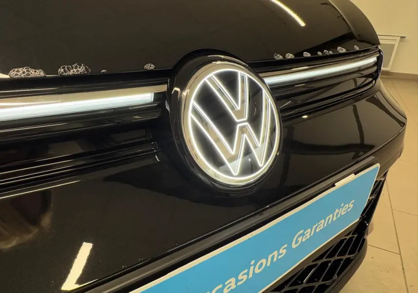 Gros plan sur la calandre avant noire grenadille d’une Volkswagen Golf 2.0 TDI avec logo VW lumineux.
