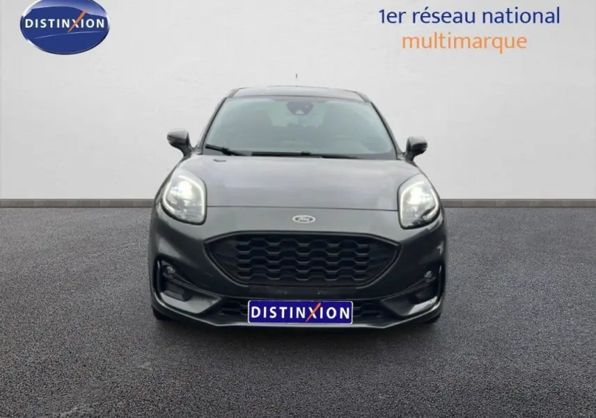 Vue avant d'un Ford Puma gris foncé 2024 avec calandre noire et phares allumés sur sol bitumé.