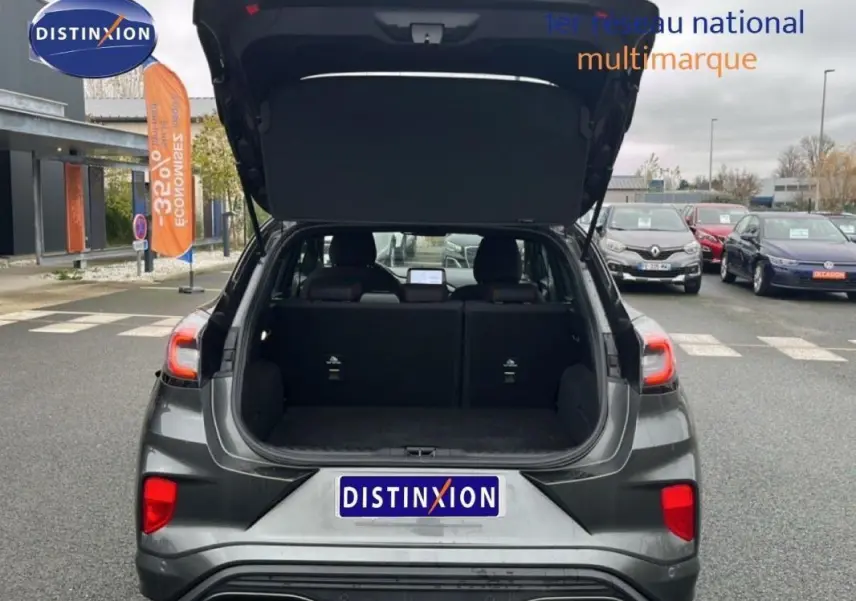 Vue arrière d'un Ford Puma gris foncé 2024 avec coffre ouvert, feux arrière allumés et jantes alliage 17 pouces visibles.