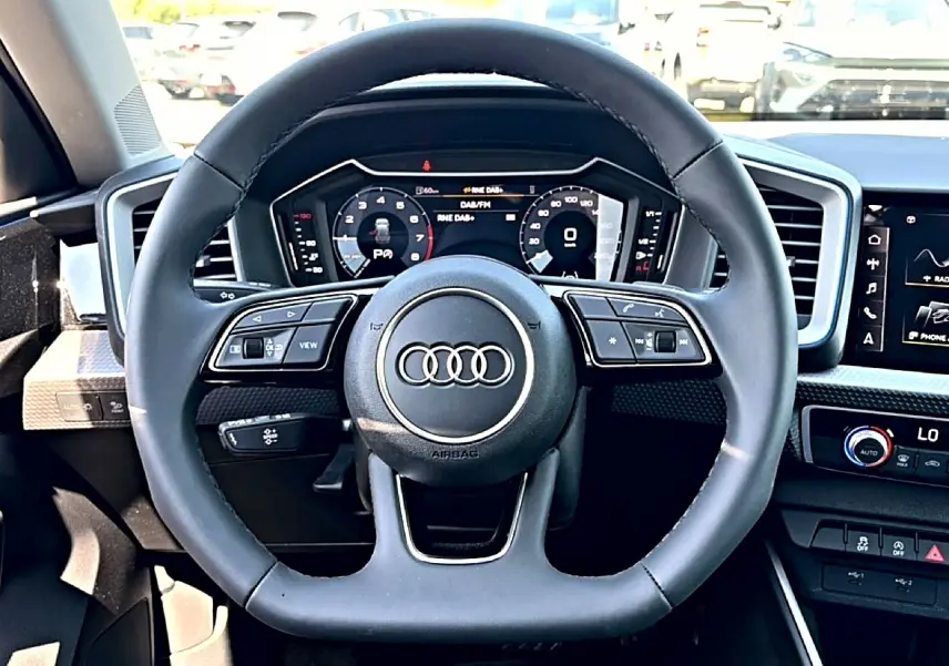 Vue frontale du volant cuir noir multifonction de l'Audi A1 Sportback avec tableau de bord numérique et écran tactile.