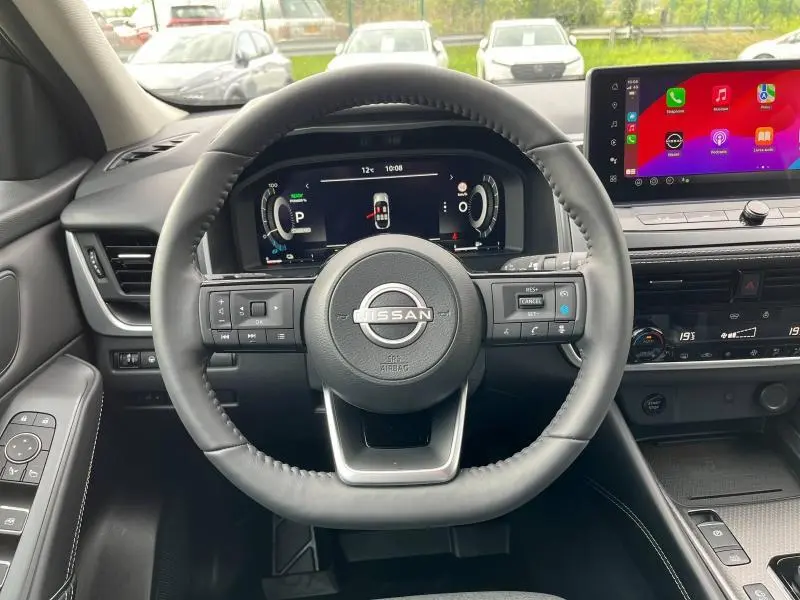Vue intérieure centrée sur le volant cuir noir du Nissan Qashqai e-POWER 2024 avec tableau de bord digital et écran tactile coloré.