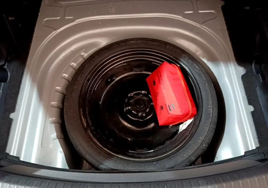 Roue de secours galette noire avec trousse de sécurité rouge dans le coffre d'une SEAT LEON gris clair 2022.