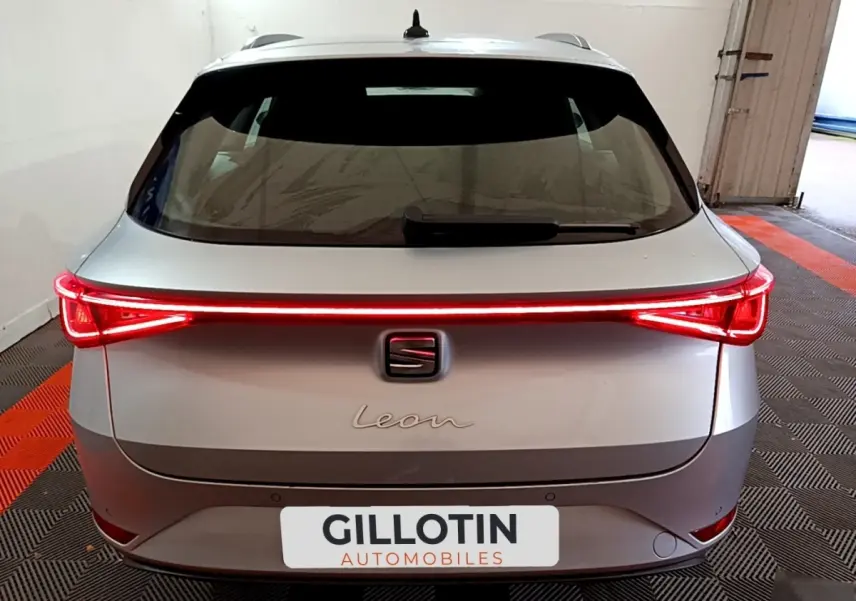 Vue arrière d'une SEAT Leon gris clair 2022 avec feux arrière LED allumés et logo central visible.