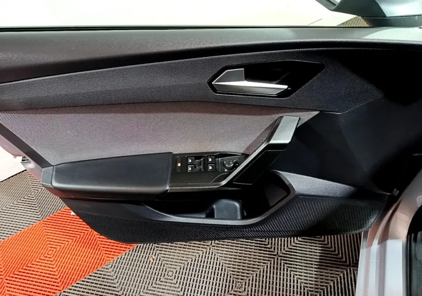 Gros plan sur la porte côté gauche d'une SEAT LEON gris clair, avec commandes électriques et poignée noire.