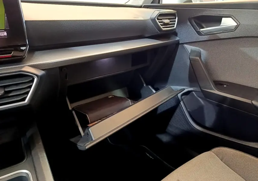 Vue intérieure côté passager du tableau de bord gris foncé avec boîte à gants ouverte et siège tissu clair d'une SEAT Leon 2022.