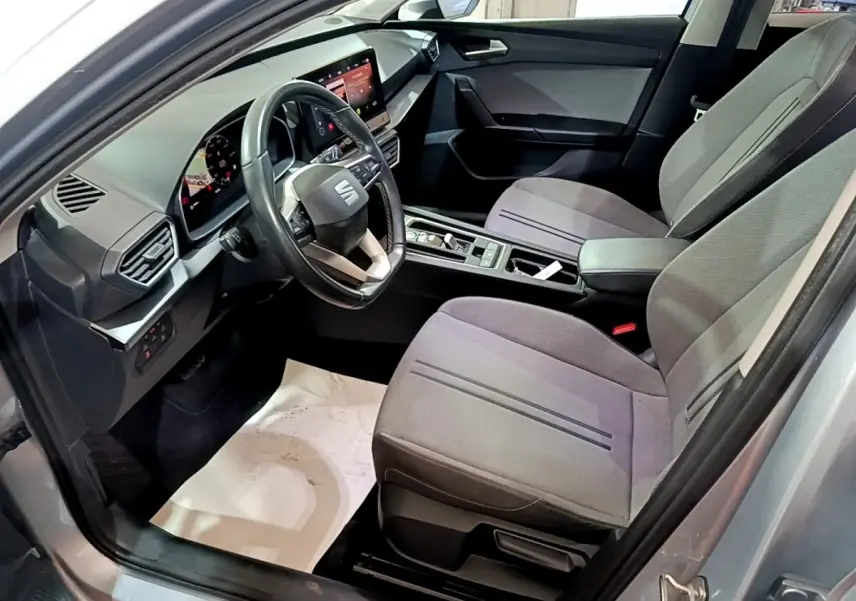 Intérieur avant droit du SEAT LEON gris clair 2022, volant cuir, écran tactile et sièges tissu gris.
