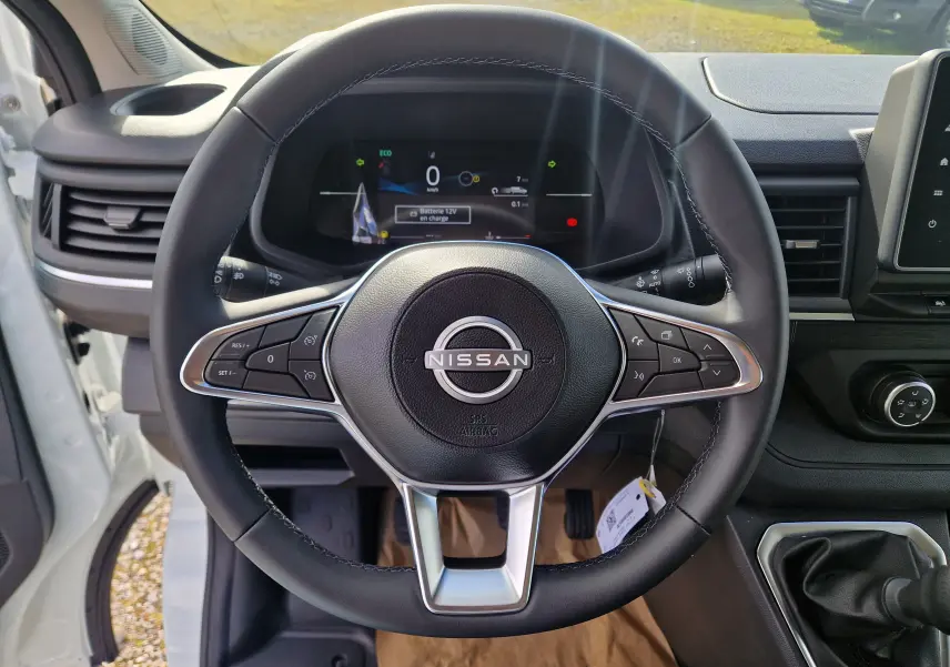 Vue intérieure centrée sur le volant noir du Nissan Primastar blanc 2025 avec tableau de bord digital et levier de vitesses manuel.