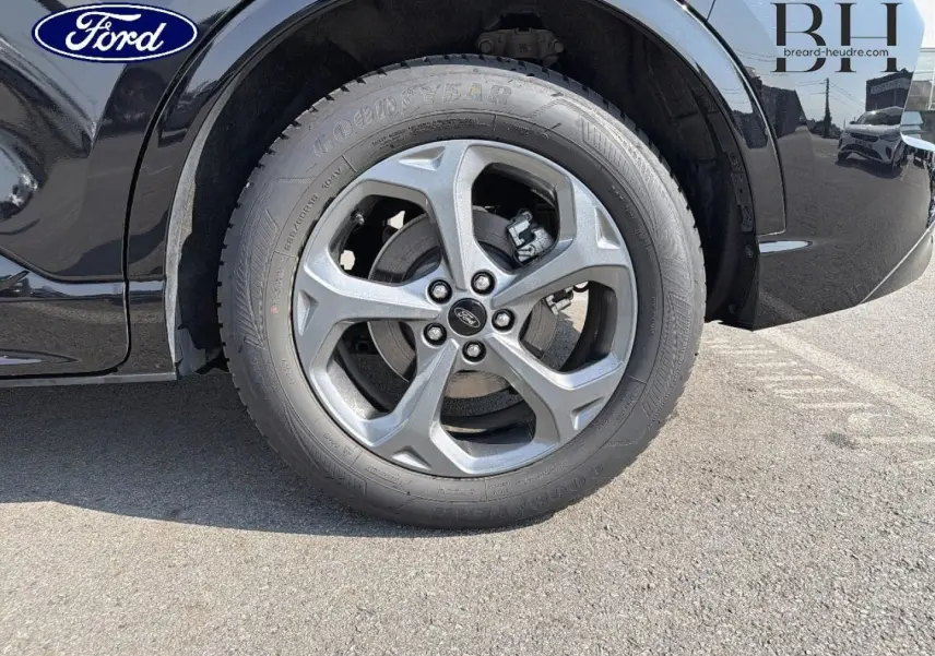 Gros plan sur la roue avant droite du Ford Kuga noir Agate Métallisée, mettant en valeur la jante alu et le logo Ford.