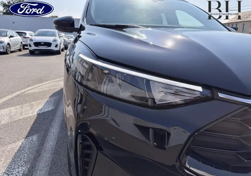 Gros plan sur l'avant droit noir Agate métallisé du Ford Kuga 2025, mettant en valeur le phare LED et la calandre sportive.