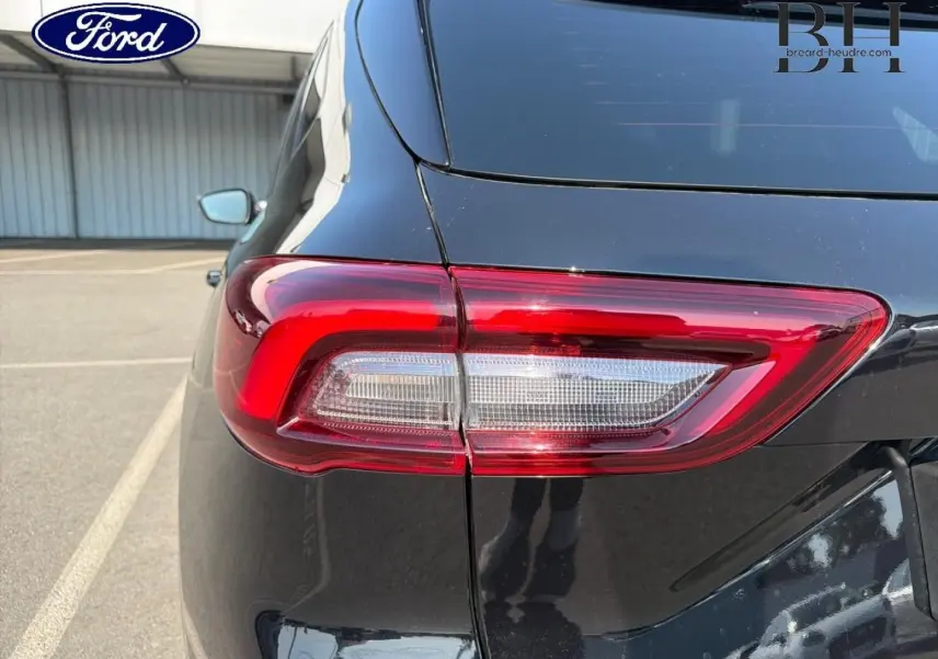 Gros plan sur le feu arrière gauche d’un Ford Kuga noir Agate Métallisée, avec reflet sur la carrosserie lisse.