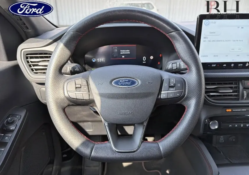 Vue rapprochée du volant en cuir noir avec surpiqûres rouges du Ford Kuga 2025, tableau de bord et écran tactile visibles.