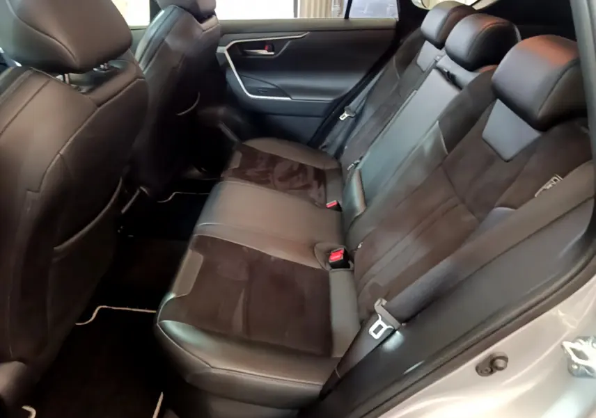Vue intérieure arrière droite du Toyota RAV4 gris clair 2019, sièges en cuir noir avec inserts alcantara et ceintures de sécurité visibles.