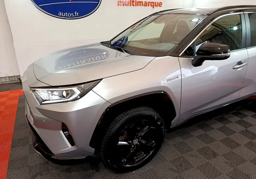 Vue 3/4 avant droit d'un Toyota RAV4 gris clair hybride avec jantes noires et badge Hybrid sur aile avant.