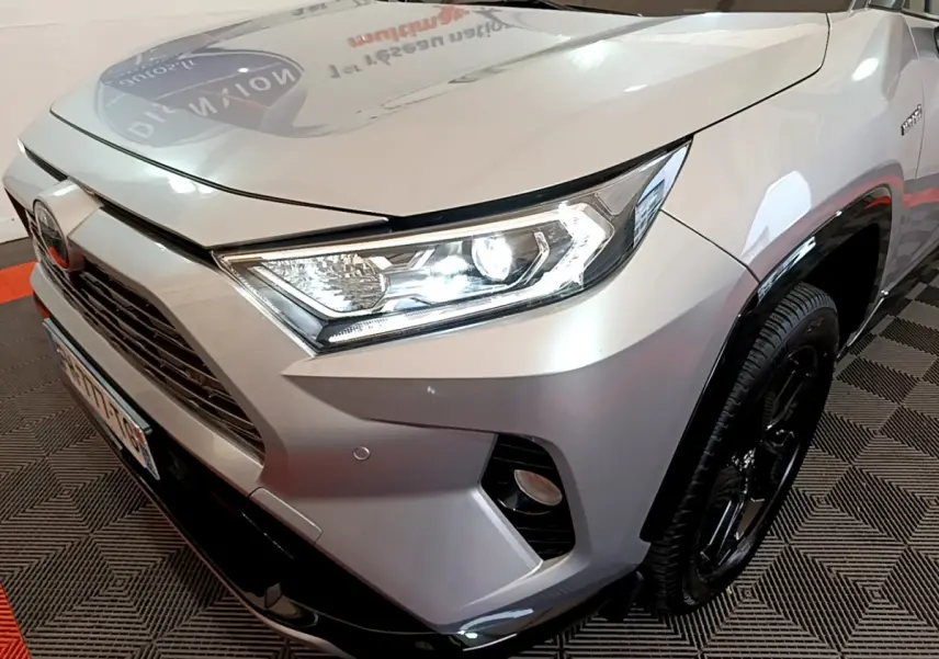 Gros plan sur l'avant droit du Toyota RAV4 gris clair 2019 avec phares LED allumés et jantes noires.