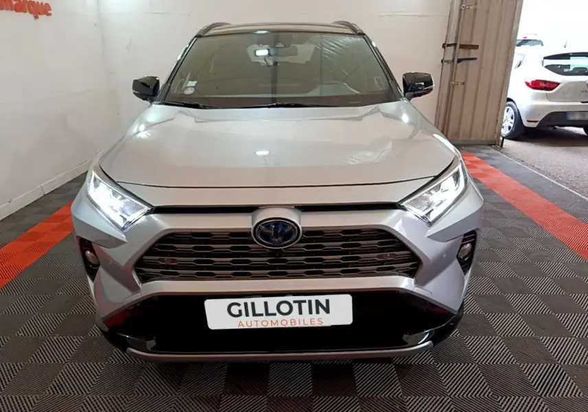 Vue frontale d'un Toyota RAV4 gris clair 2WD 218ch avec calandre noire et phares LED allumés dans un garage.