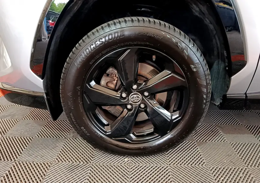 Gros plan sur la roue avant gauche du Toyota RAV4 gris clair, jante alliage noir brillant avec logo Toyota central.