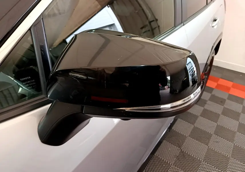 Rétroviseur noir en gros plan côté gauche d'un Toyota RAV4 gris clair, avec clignotant intégré visible.
