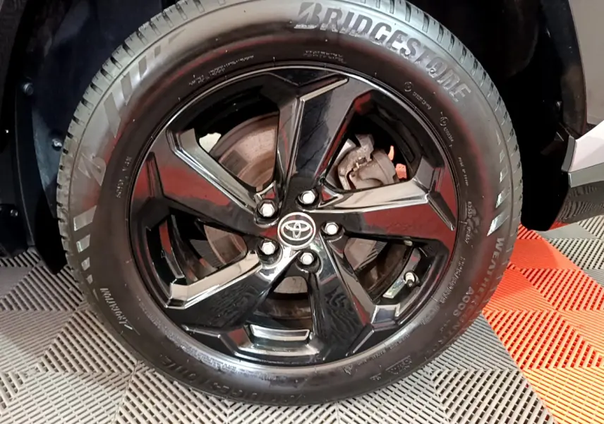 Gros plan sur la roue avant droite du Toyota RAV4 gris clair, jante noire brillante avec logo Toyota central.