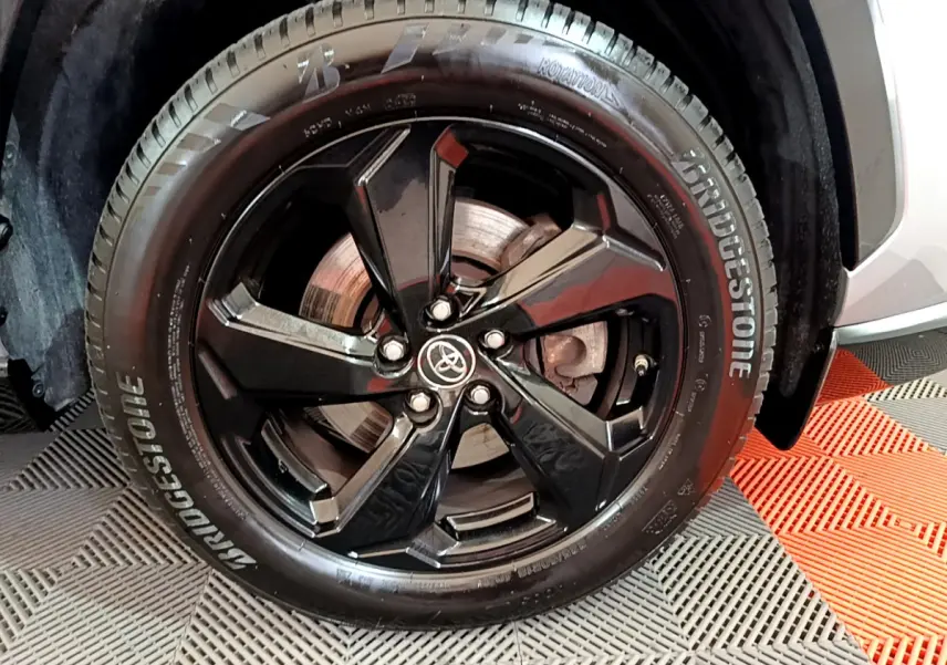 Gros plan sur la roue avant droite du Toyota RAV4 gris clair, jante noire brillante avec logo Toyota central.