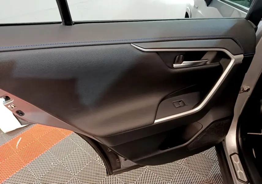 Porte arrière droite ouverte d’un Toyota RAV4 gris clair, montrant le panneau intérieur noir avec insert argenté.