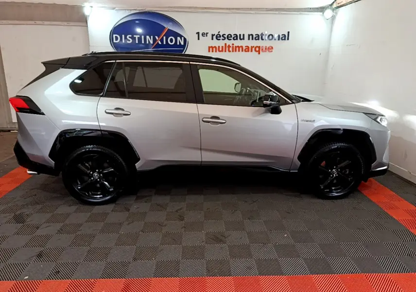 Profil côté droit d'un Toyota RAV4 gris clair 2WD 218ch Collection avec jantes noires et toit noir en showroom.