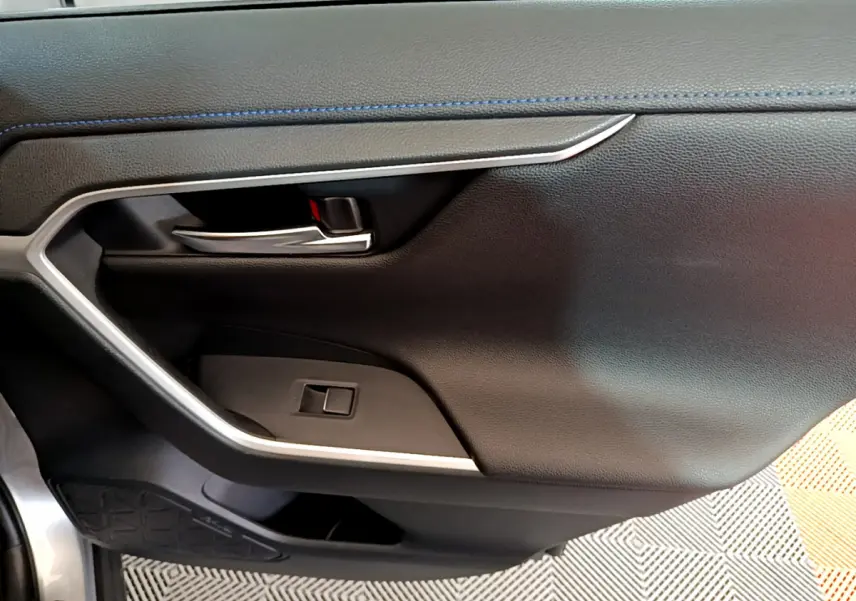 Détail de la porte intérieure côté gauche du Toyota RAV4 gris clair avec poignée chrome et surpiqûres bleues.