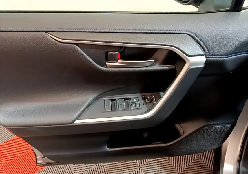 Gros plan sur la porte intérieure côté conducteur du Toyota RAV4 gris clair, avec commandes de vitres et poignée argentée.