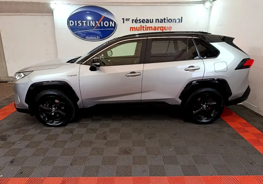 Profil côté gauche d'un Toyota RAV4 gris clair 2WD 218ch Collection avec jantes noires en intérieur showroom.