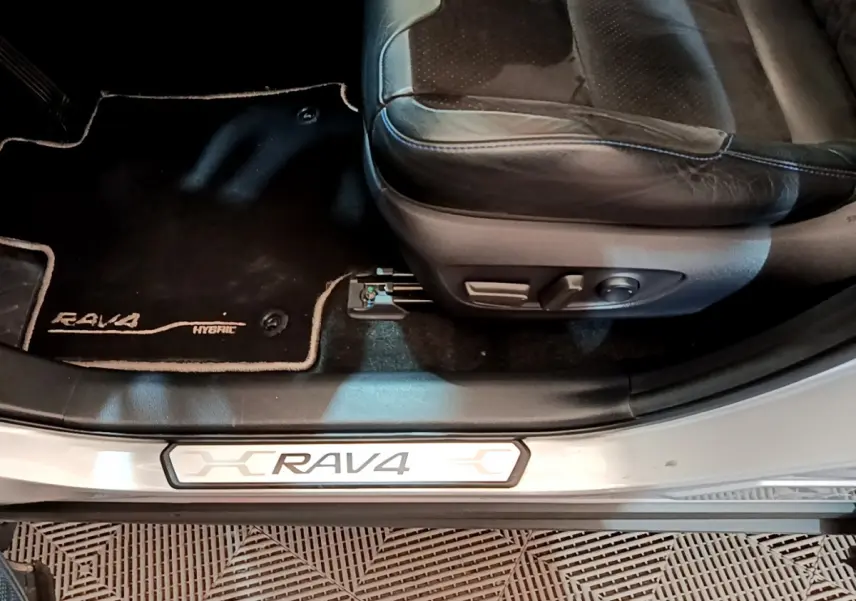 Détail intérieur côté conducteur du Toyota RAV4 gris clair, montrant siège en cuir et tapis avec logo Hybrid.