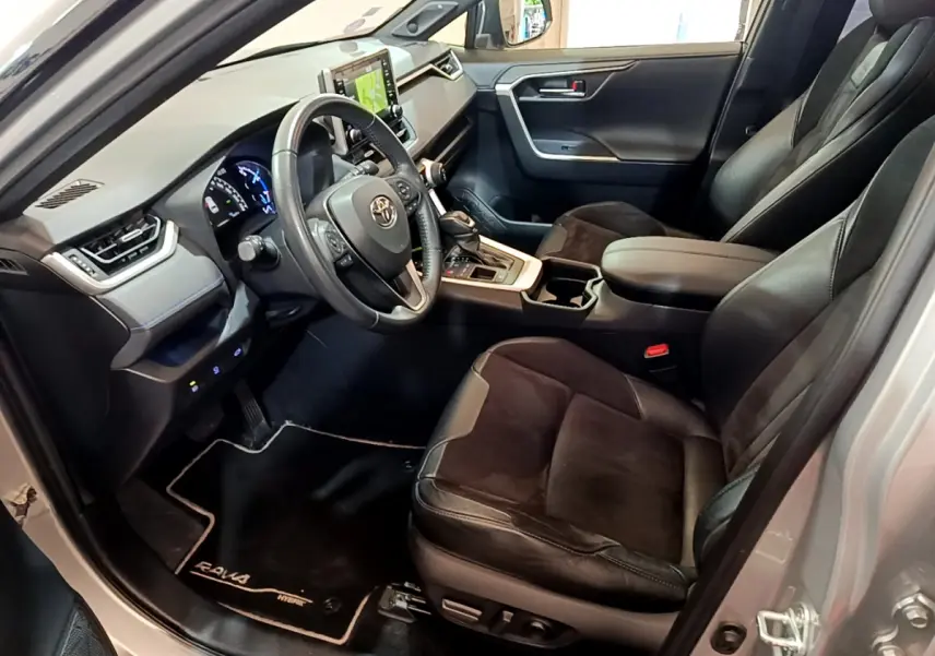 Intérieur du Toyota RAV4 gris clair vu côté conducteur, sièges cuir noir et tableau de bord moderne avec écran tactile.