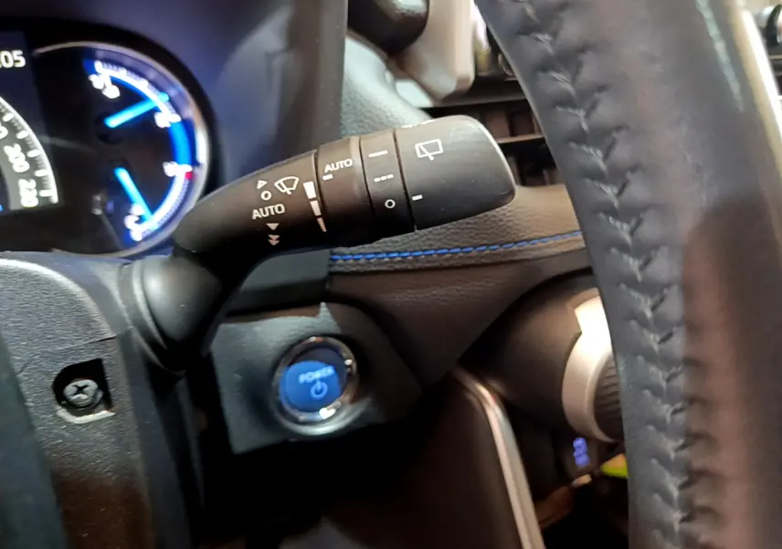 Gros plan intérieur sur la manette d'essuie-glace et bouton start bleu du Toyota RAV4 gris clair 2019 côté gauche du volant.