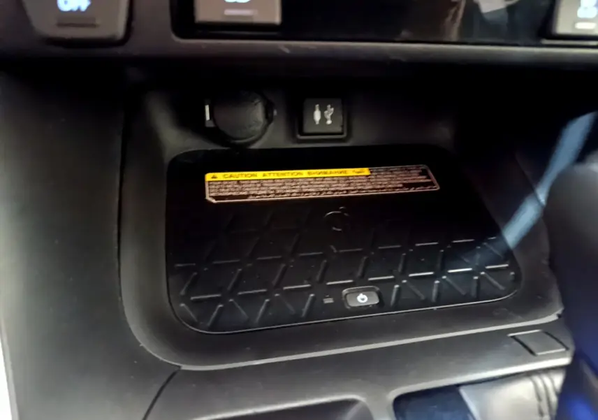 Gros plan sur la zone de recharge sans fil noire du Toyota RAV4 gris clair, avec prise USB et bouton tactile visible.
