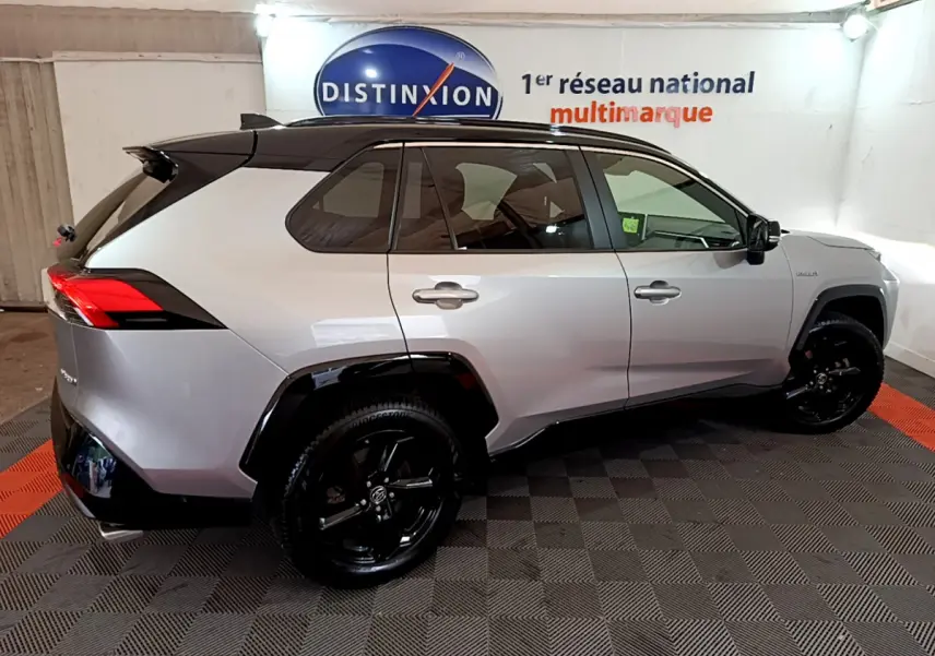 Vue de profil côté gauche d'un Toyota RAV4 2WD gris clair avec toit noir et jantes noires dans un showroom.