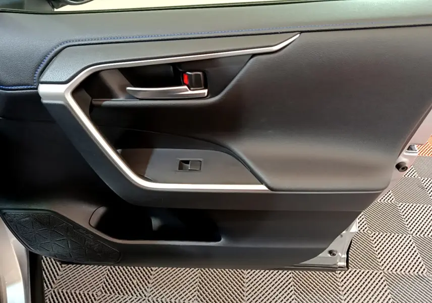Gros plan sur la porte intérieure côté conducteur du Toyota RAV4 gris clair, avec poignée argentée et haut-parleur intégré.