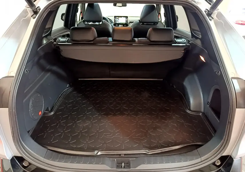 Coffre ouvert d'un Toyota RAV4 gris clair, vue arrière montrant la surface de chargement avec tapis caoutchouc marqué RAV4.