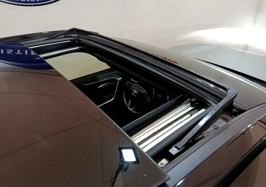 Toit ouvrant panoramique ouvert sur un Toyota RAV4 gris clair, vue plongeante sur l'intérieur côté conducteur.