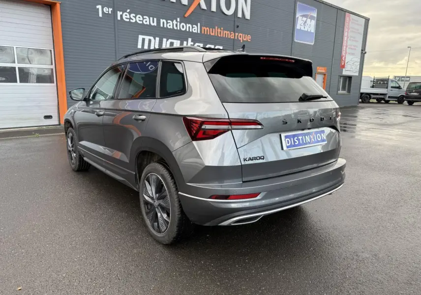 Vue 3/4 arrière droite d'un Skoda Karoq gris graphite métallisé avec jantes alliage noires et toit ouvrant panoramique électrique.